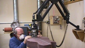 Here you see Jim in action routing the binding ledge. An articulating arm holds the router in a fork attached to its end. Jim scavenged the fork from one of his kids' old bikes! Also visible is a custom-made table for holding the body in place during the operation