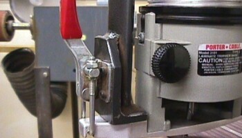 A close-up of the clamp holding the router in place in the fork. One side of the fork is visible. Also visible supporting the router from the bottom is a metal routing guide Jim made on the Fadal