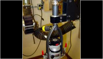 The router attaches in an old bicycle fork adapted to hold it. The fork is mounted in an articulating arm that keeps the router vertical so that it can cut the binding ledges on the arched guitar back.