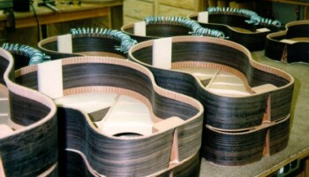 The bodies in the back have linings being glued in place, held by dozens of small clamps. The bodies in front have lining already in place. Top braces and dovetails for attaching necks are also visible here